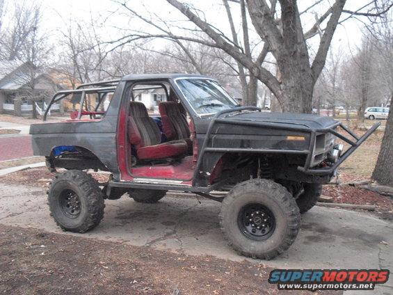 Modified SUV with roll cage, large tires, and custom bumper. Doors are removed, showing red interior seats
