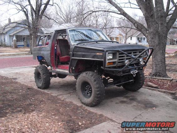 Black modified Ford Bronco with off-road tires, roll cage, and custom bumper