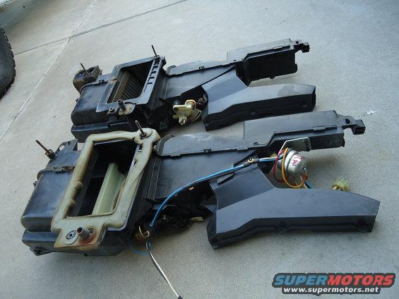 Two black plastic HVAC assemblies with wires and metal components, laid out on a concrete surface