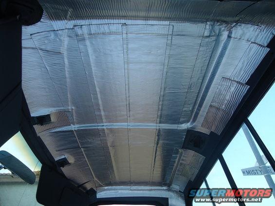 Vehicle interior ceiling covered in silver soundproofing material, showing insulation panels and some structural beams