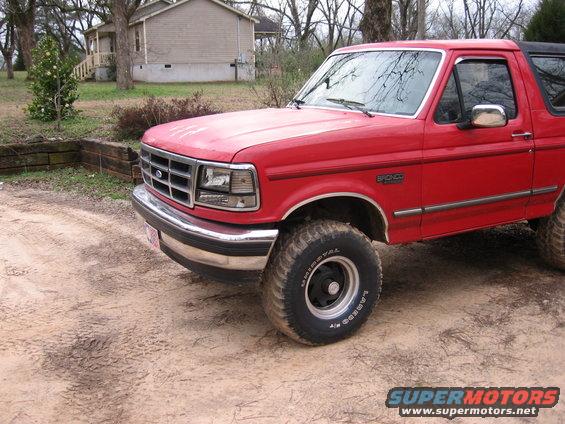 Red 1993 Ford Bronco parked on a dirt road in front of a house