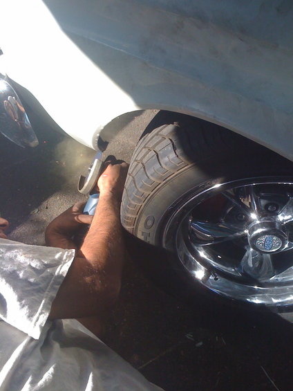 Person's hands working on a chrome wheel and tire of a light-colored vehicle