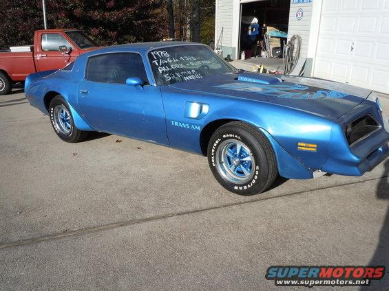 Blue 1978 Pontiac Trans Am with hood decal, parked on concrete, with a red pickup truck behind it