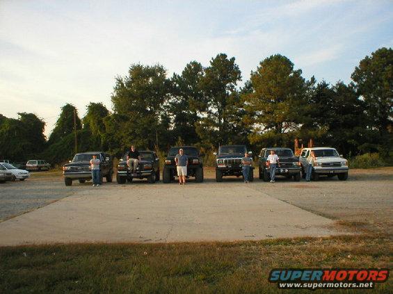 Several pickup trucks and SUVs parked in a lot with trees in the background