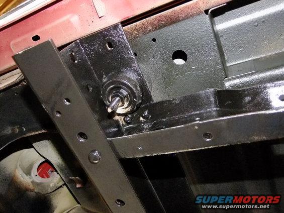 Close-up of a black metal bracket attached to a vehicle's frame, with a bolt and nut visible