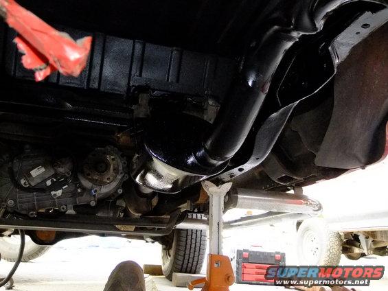 Underside of a vehicle on jack stands, showing drivetrain and exhaust components. A red toolbox is visible