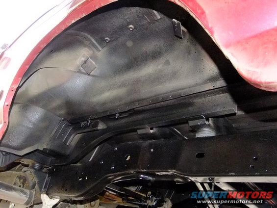 Red vehicle's rear chassis and wheel well, showing black undercoating