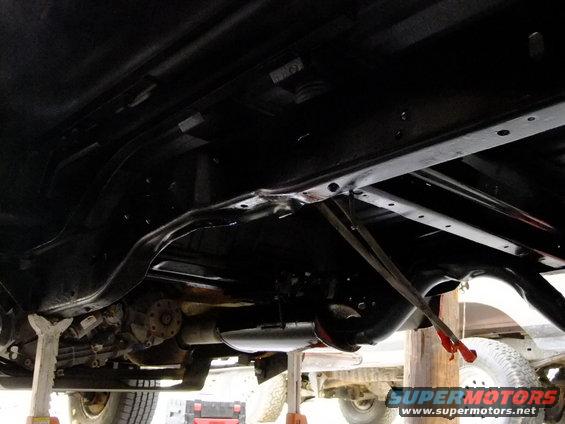 Underside of a vehicle on jack stands, showing the frame, exhaust, and drivetrain components