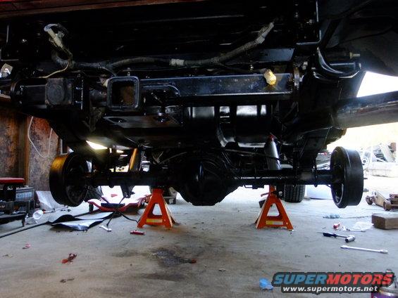 Underside of a vehicle on jack stands, showing the rear axle, suspension, and hitch receiver