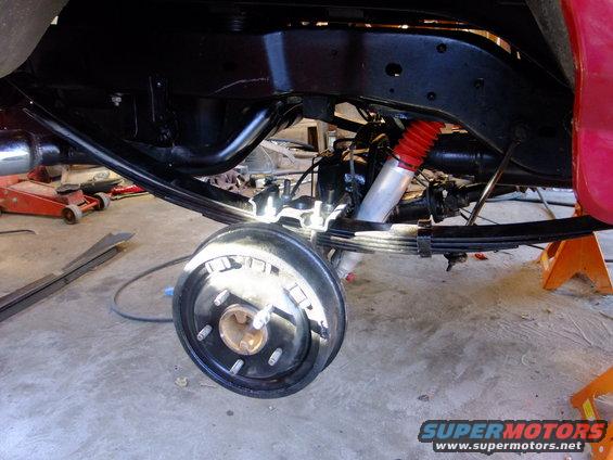 Rear axle assembly with leaf springs and red-accented shock absorber, viewed from the side