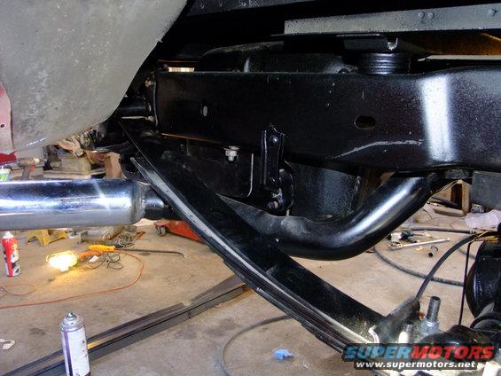 Underside of a vehicle showing the rear suspension, leaf springs, and frame. Tools and equipment are visible in the background