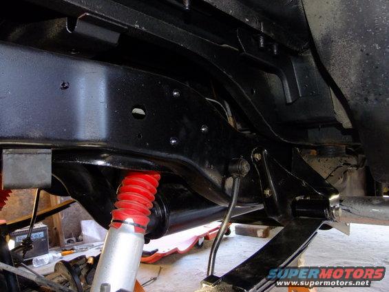 Close-up of a vehicle's rear suspension and frame, showing red coilover shocks and black painted metal components