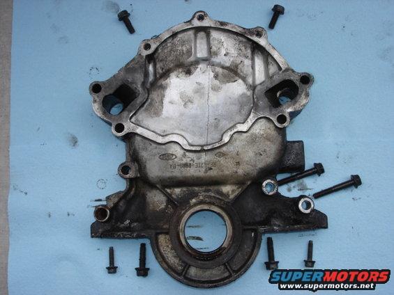 Dirty metal engine timing cover with Ford logo and part number visible, surrounded by bolts on a blue cloth