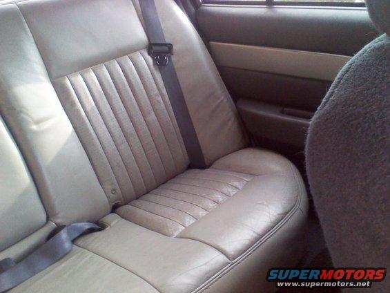 Rear bench seat with beige leather upholstery and a seatbelt. Door panel visible on the right