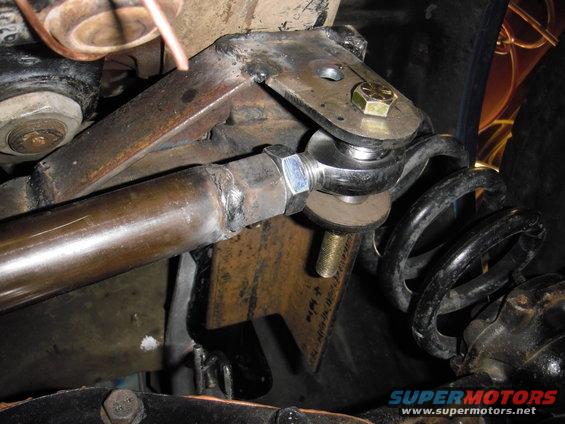 Close-up of a vehicle's suspension system, showing a metal rod connected to a joint and a coil spring