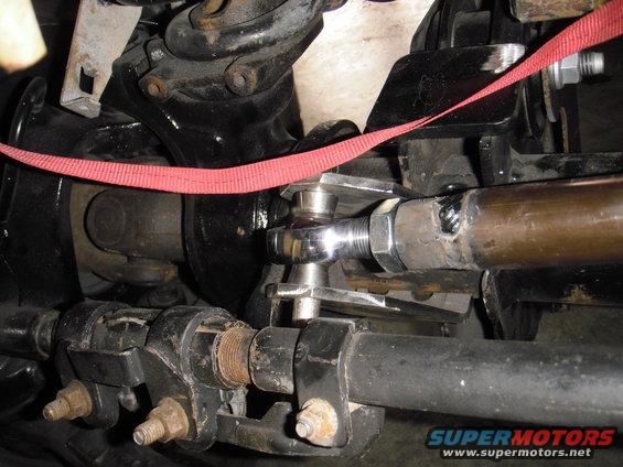 Close-up of vehicle steering linkage with a red strap, showing metal parts and bolts