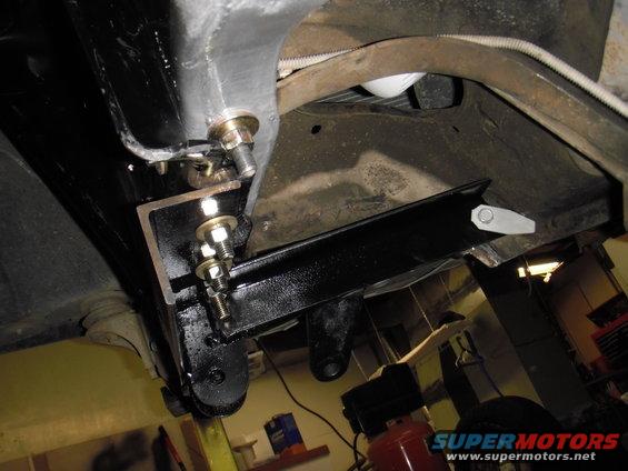 Underside of a vehicle showing black aftermarket brackets bolted to the frame, with some suspension components visible