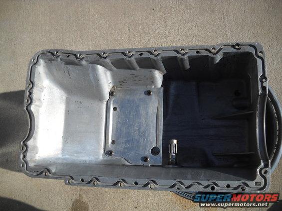 Aluminum oil pan with a metal plate bolted on, resting on a concrete surface