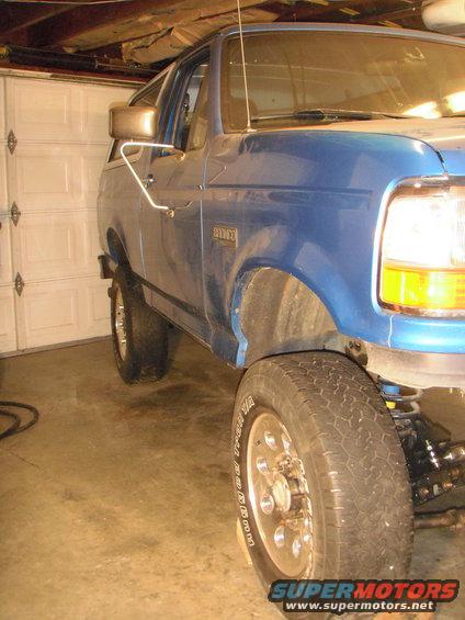 Blue SUV parked in garage, front fender and wheel visible. Badge reads 2000