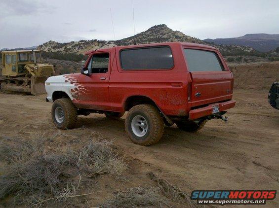 Red SUV with white front fender and flame decals parked on dirt road. Yellow bulldozer in background