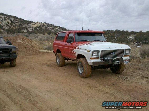 Red and white 1978 Ford Bronco with flame decals and a winch, parked on a dirt road