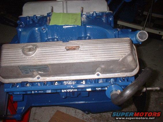 Blue engine block with silver ribbed valve covers. A green piece of tape is on top of the intake manifold
