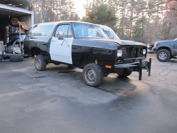 Black and white SUV with missing grille, parked outside a garage