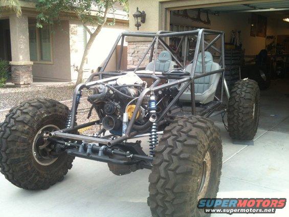 Custom off-road buggy with roll cage, large tires, and exposed engine, parked in a driveway