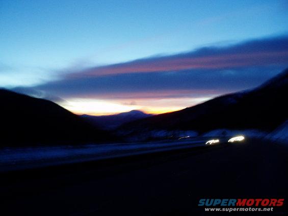 Headlights streak across a dark highway during a colorful dusk sky