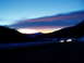 2009 Kenworth T800 - Headlights blur on a highway as the sun sets, painting the sky with vibrant colors.