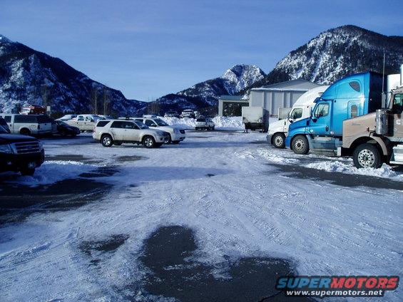 Trucks and SUVs parked in a snow-covered lot with mountains in the background