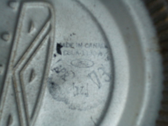 Close-up of a Ford emblem with 'MADE IN CANADA' and part numbers visible