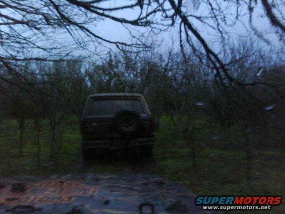 SUV parked in a field with trees around it. Spare tire mounted on the rear door