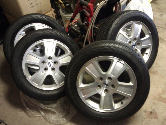 Four silver alloy wheels with tires, each with a Ford logo in the center