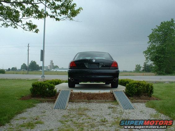 Black sedan parked on a concrete pad with ramps. Cloudy sky