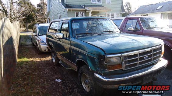 Green Ford Bronco with damaged front fender, parked next to a silver SUV and a maroon truck