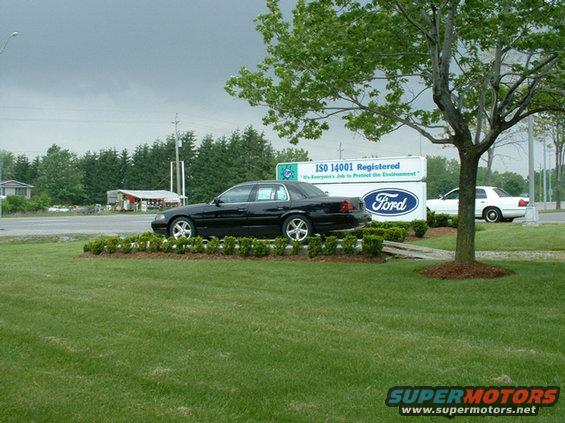 Black 2000 Ford Crown Victoria parked on grass, side view. White Ford Crown Victoria in background
