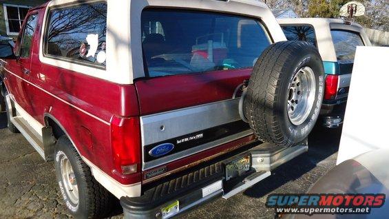Red and white Ford Bronco with a spare tire mounted on the rear, parked next to another SUV
