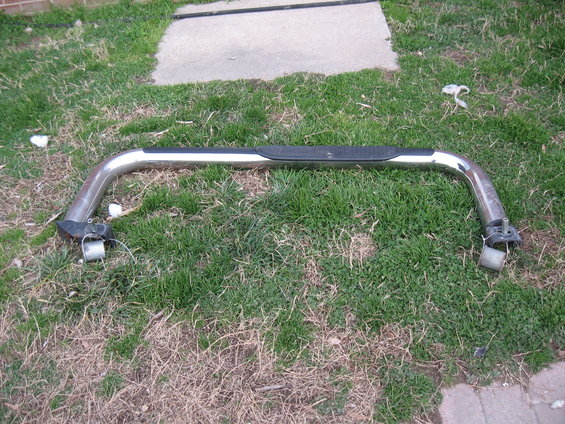 Chrome nerf bar with black step pad, detached from vehicle, lying on grass
