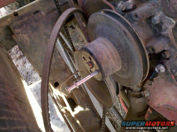 Close-up of a rusty engine pulley with a V-belt. A bolt is inserted into the pulley hub
