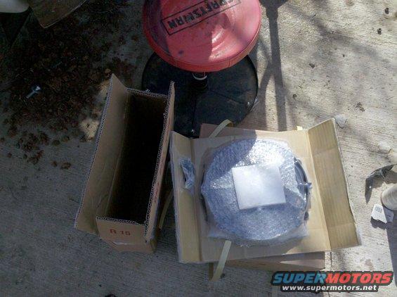 Car part wrapped in bubble wrap inside a cardboard box on concrete