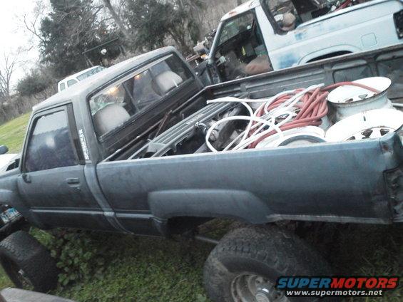 Side view of dark blue pickup truck bed loaded with coiled hoses and spare tires