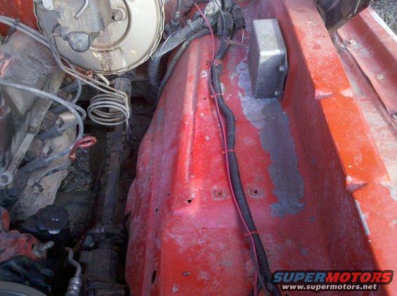 Red engine bay with brake booster, wiring, and steering column visible