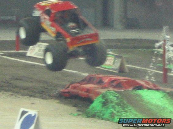 Red monster truck mid-air over a dirt ramp