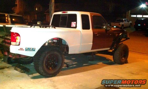 Pickup truck with white cab and bed, brown front clip, lifted suspension, and large tires