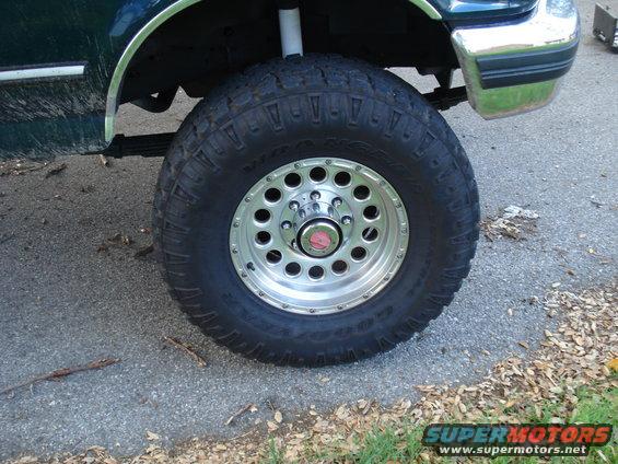 Green truck fender and large off-road tire with chrome rim on asphalt