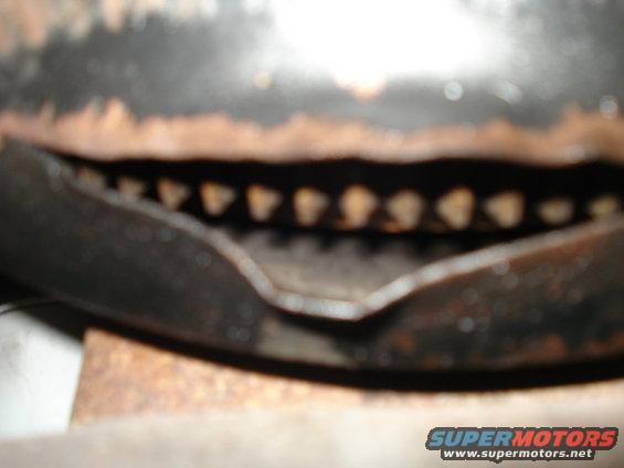 Close-up of a rusty, dark-colored grille section with visible teeth-like openings