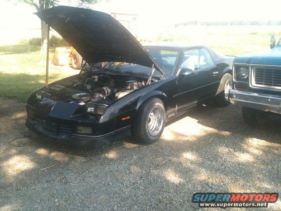 1988 Chevrolet Camaro parked next to a pickup truck, hood is open showing the engine