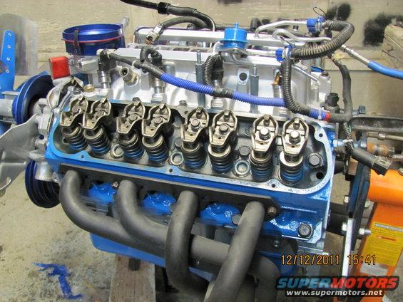 Engine with blue valve covers and black exhaust manifolds, mounted on an orange stand