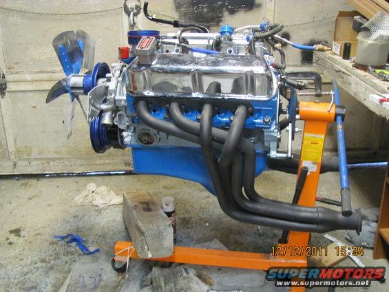V8 engine on an orange stand, chrome valve covers, black headers, blue block, and a fan